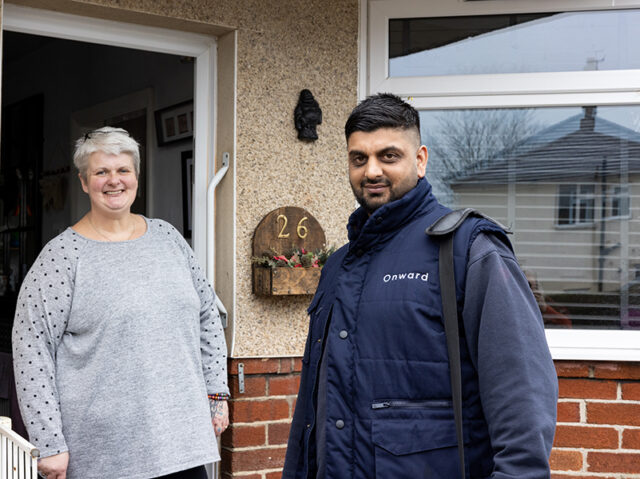 Photograph of a woman standing in the open doorway of her come, smiling at the camera. She is with an Onward employee who stands outside, also smiling at the camera.