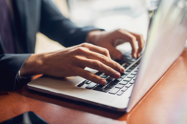 Photograph showing close-up of hands typing on laptop keyboard, suggesting work or communication activity. Focus on fingers and keys with blurred background.