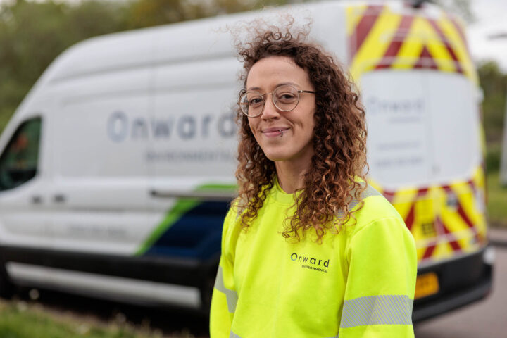 Photograph showing a person wearing a bright yellow high-visibility Onward International sweatshirt standing in front of a white Onward International van with blue and green accents and red-yellow chevron markings on the rear. The image highlights branding on both the clothing and vehicle, suggesting a work or service context related to the company.