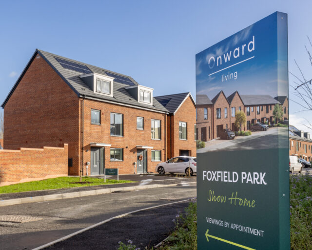 Image depicting a street with a row of houses, and a sign that reads 'Onward living, Foxfield Park Dream Home'.