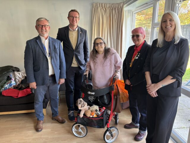 Four Onward Homes staff members smiling alongside an elderly resident with a wheeled walker indoors.